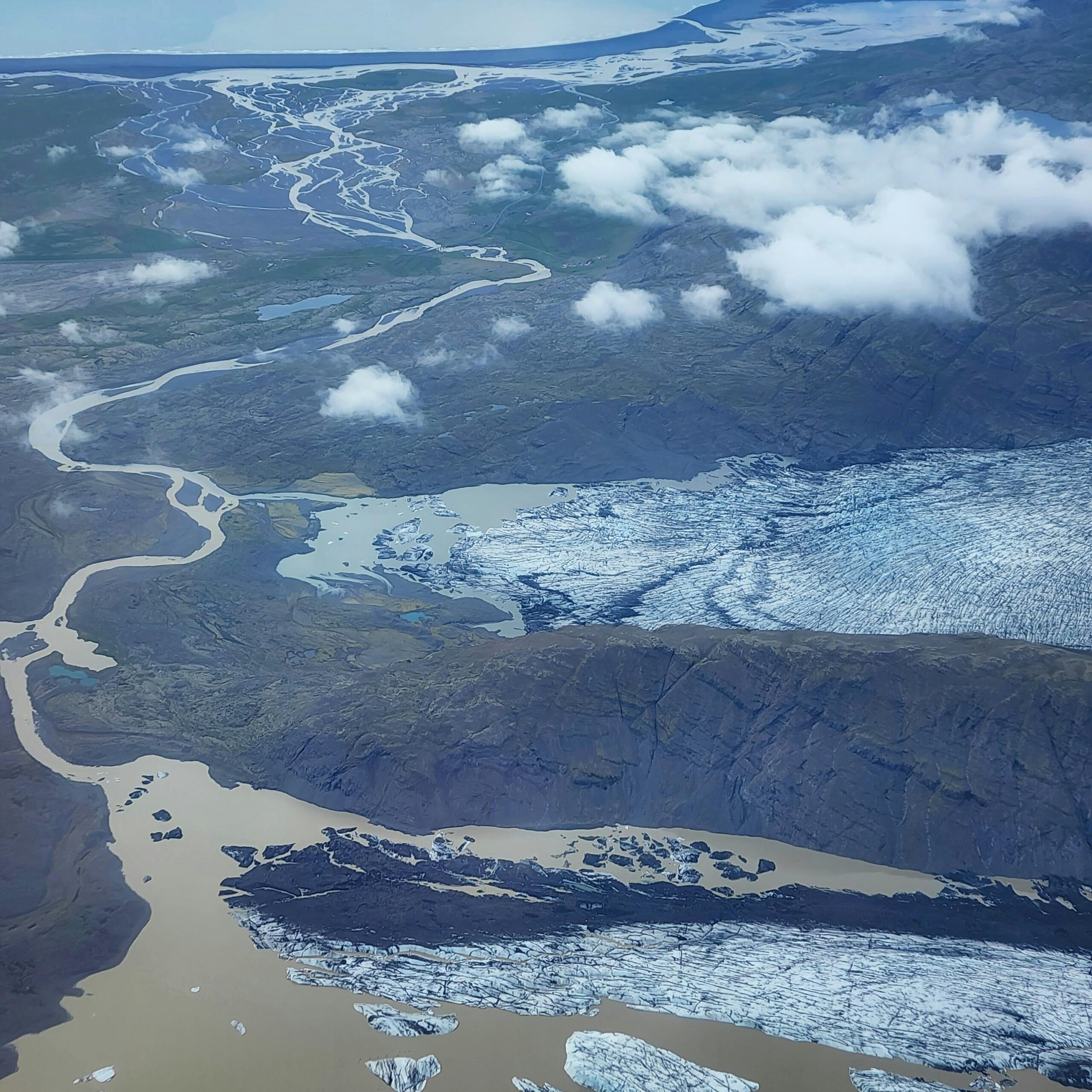 Stunning aerial photograph of a glacier in Iceland showing rivers and ice formations beneath clouds.